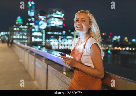 Junge Frau in London bei Nacht mit ihrem Smartphone Stockfoto