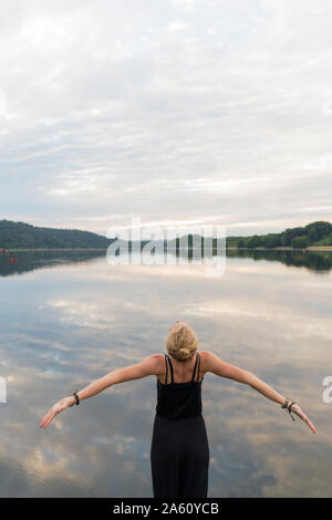 Junge Frau an einem See mit ausgestreckten Armen Stockfoto