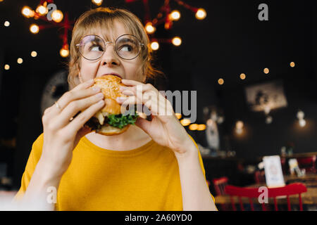 Junge Frau Burger essen in einem Restaurant Stockfoto