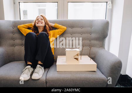 Gerne Frau sitzt auf der Couch neben architektonischen Modell Stockfoto