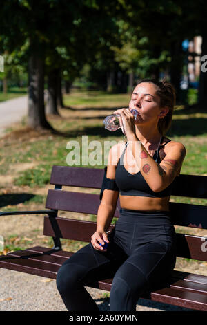 Sportliche junge Frau mit einem kühlen Pause auf der Parkbank Stockfoto