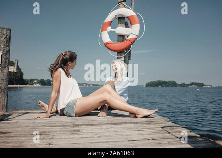 Mutter und Tochter sitzen am Bootsanleger, Entspannen am Meer Stockfoto