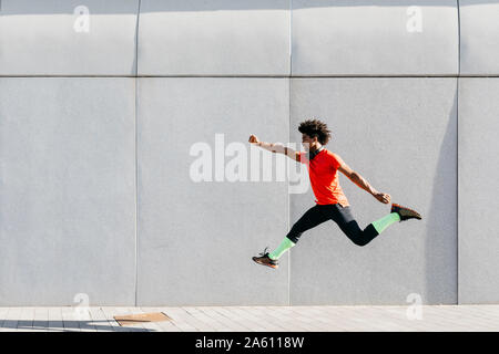 Junger Mann springt mit einer grauen Wand im Hintergrund Stockfoto