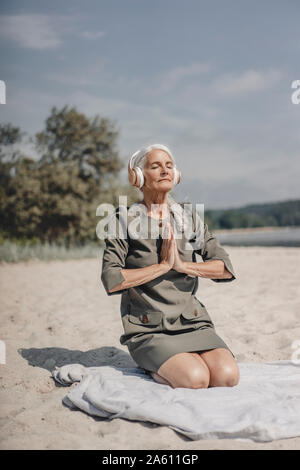 Ältere Frau, Meditieren mit Kopfhörern am Strand Stockfoto