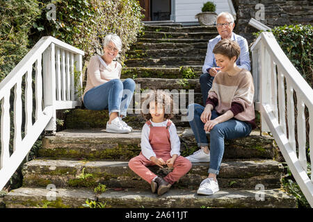 Älteres Ehepaar mit erwachsener Tochter und Enkel sitzt auf der Treppe im Garten ihres Hauses Stockfoto