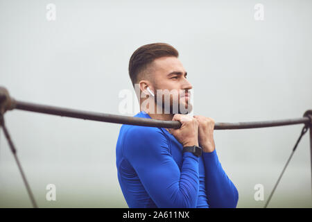 Ein bärtiger Kerl, Pull-ups auf einen horizontalen Balken in einem Stadion im Nebel. Stockfoto