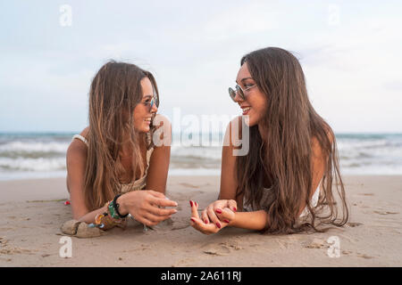 Zwei glückliche weibliche Freunde am Strand liegen im Gespräch Stockfoto