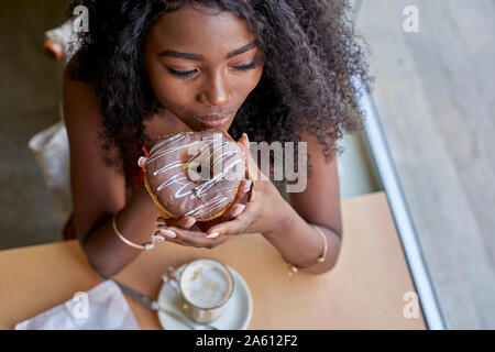 Porträt der jungen afrikanischen Frau essen einen Donut in einem Cafe Stockfoto