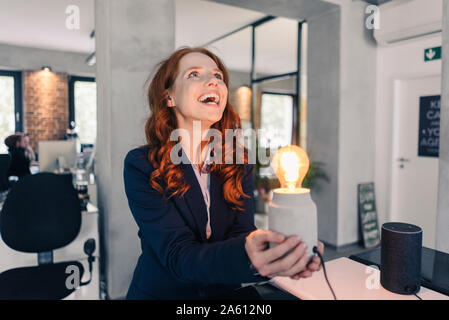 Lachende rothaarige Geschäftsfrau holding Lampe im Büro Stockfoto