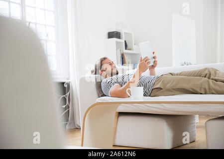 Junger Mann liegt auf der Couch zu Hause mit der Tablette Stockfoto
