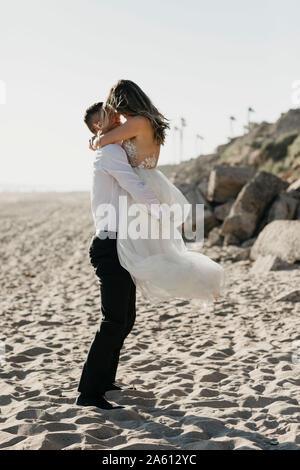 Glückliche Braut und Bräutigam umarmen am Strand Stockfoto