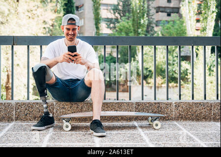 Lächelnden jungen Mann mit beinprothese und Sie ihr Smartphone skateboard Stockfoto