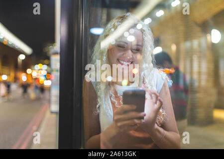 Junge Frau in London bei Nacht Blick auf Ihr Smartphone und Warten auf den Bus Stockfoto