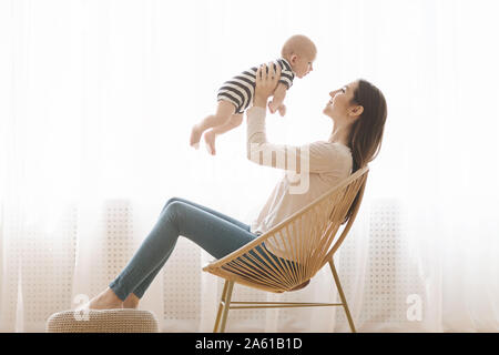 Die Mutter sitzt im korbstuhl und Spielen mit Neugeborenen Stockfoto