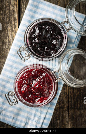 Heidelbeere und Himbeere Marmelade im Glas auf kariert Serviette. Ansicht von oben. Stockfoto
