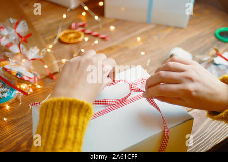 Weihnachten Komposition mit vorhanden. Das Mädchen bindet eine rote Schleife auf die Geschenkbox. Stockfoto