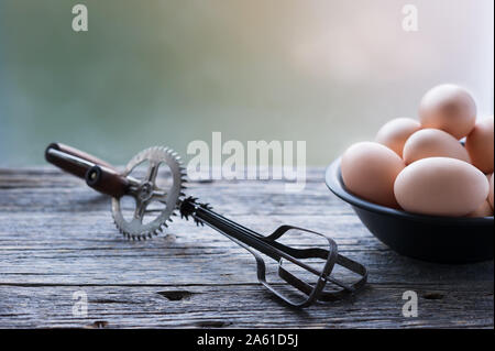 Altes ei Schneebesen Mixer und eine Schüssel mit Bio Eier im rustikalen Holztisch verwitterten grauen Hintergrund. Selektive konzentrieren. Horizontal, mit kopieren. Stockfoto