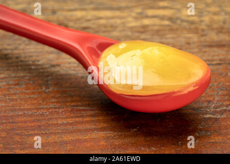 Raw Honig auf ein rotes Steinzeug Teelöffel gegen Grunge rustikalem Holz Stockfoto