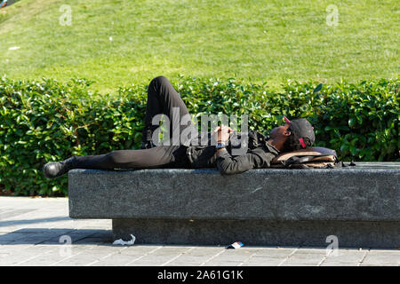 Beyoglu, Türkei - 20. Oktober 2019: jungen afrikanischen Mann mit Baseball Hut und schwarzer Kleidung schlafen auf eine konkrete Bank bei öffentlichen Park in Istanbul Stockfoto