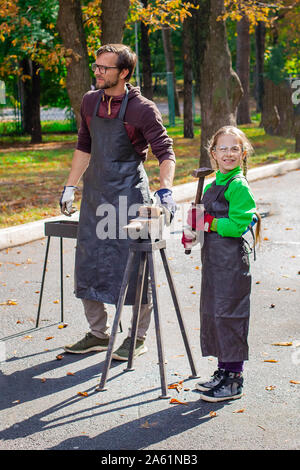 Vater und Kind sind im Handwerk tätig. Ein Schmied schmiedet eine Metall blank auf dem Amboss auf einer Messe in Anwesenheit von Zuschauern. Close-up. Stockfoto