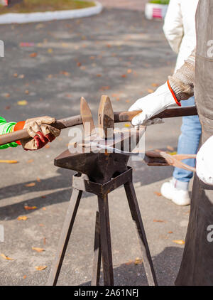 Vater und Kind sind im Handwerk tätig. Ein Schmied schmiedet eine Metall blank auf dem Amboss auf einer Messe in Anwesenheit von Zuschauern. Close-up. Stockfoto