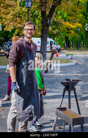 Vater und Kind sind im Handwerk tätig. Ein Schmied schmiedet eine Metall blank auf dem Amboss auf einer Messe in Anwesenheit von Zuschauern. Close-up. Stockfoto