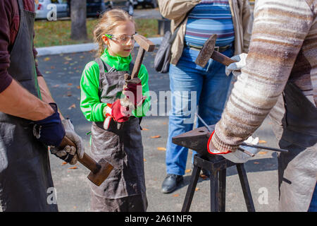 Vater und Kind sind im Handwerk tätig. Ein Schmied schmiedet eine Metall blank auf dem Amboss auf einer Messe in Anwesenheit von Zuschauern. Close-up. Stockfoto