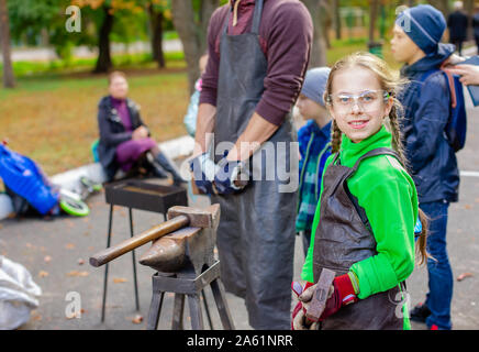 Vater und Kind sind im Handwerk tätig. Ein Schmied schmiedet eine Metall blank auf dem Amboss auf einer Messe in Anwesenheit von Zuschauern. Close-up. Stockfoto