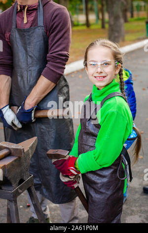 Vater und Kind sind im Handwerk tätig. Ein Schmied schmiedet eine Metall blank auf dem Amboss auf einer Messe in Anwesenheit von Zuschauern. Close-up. Stockfoto