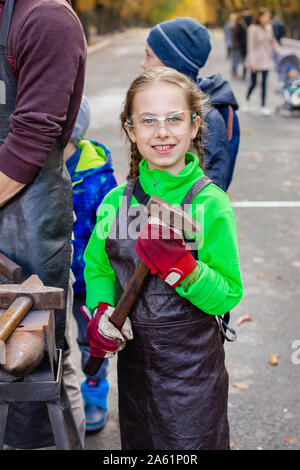 Vater und Kind sind im Handwerk tätig. Ein Schmied schmiedet eine Metall blank auf dem Amboss auf einer Messe in Anwesenheit von Zuschauern. Close-up. Stockfoto