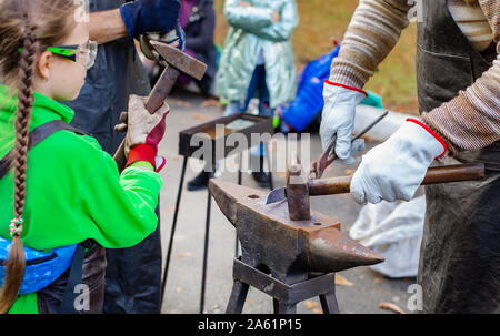 Vater und Kind sind im Handwerk tätig. Ein Schmied schmiedet eine Metall blank auf dem Amboss auf einer Messe in Anwesenheit von Zuschauern. Close-up. Stockfoto