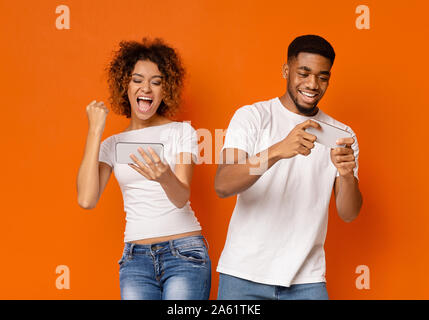 Emotionale afrikanische amerikanische Mann und Frau spielen auf Smartphones Stockfoto