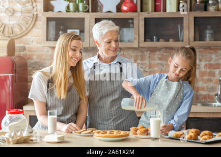 Süße Mädchen gießt Milch an Oma und Mama in der Küche Stockfoto