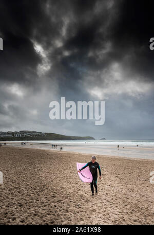 Ein Surfer zu Fuß auf den Fistral Beach als dunkle Sturmwolken über die Küste in Newquay in Cornwall. Stockfoto
