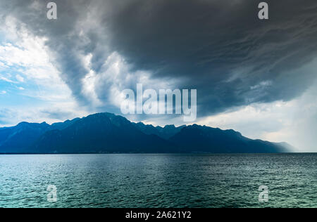 Blick auf die Alpen, den Genfer See und dunkle Regenwolken vor Regen. Schuß vom Ufer des Sees in Montreux, Schweiz. Stockfoto