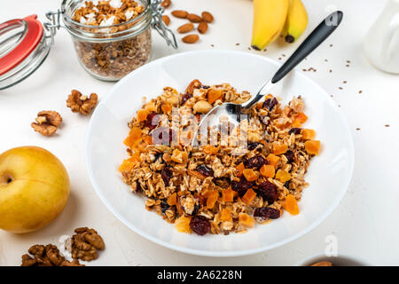 Frühstück mit Müsli Müsli mit Milch, getrocknete Aprikosen, Preiselbeeren, Mandeln und Leinsamen in der Schüssel auf einem weißen Hintergrund. Gesundes Müsli Frühstück. Stockfoto