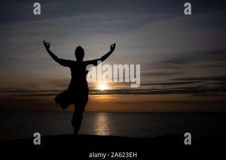 Silhouette einer Frau bei Sonnenuntergang, Yoga Position gegen die untergehende Sonne auf der Insel Bornholm, Dänemark, Yoga bei Sonnenuntergang auf der Insel Stockfoto