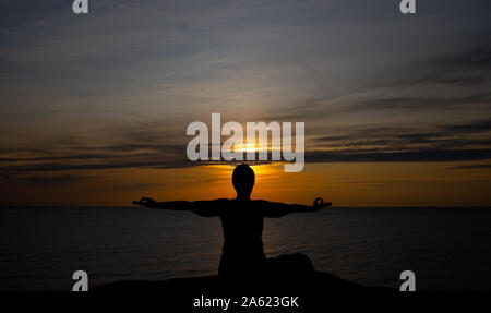 Silhouette einer Frau bei Sonnenuntergang, Yoga Position gegen die untergehende Sonne auf der Insel Bornholm, Dänemark, Yoga bei Sonnenuntergang auf der Insel Stockfoto
