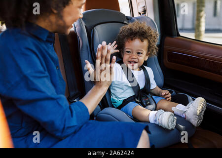 Junge Mutter spielt mit ihrem Sohn im Auto. Zwei Leute sitzen auf einem Rücksitz. Stockfoto