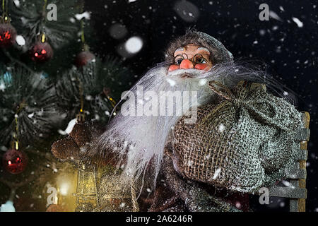 Santa Claus im Freien neben dem Weihnachtsbaum in Schneefall Geschenke für Kinder. Frohe Weihnachten & Silvester Konzept Stockfoto