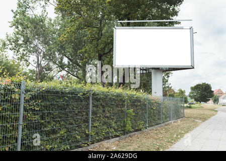 Leere Weiße und isolierte Mockup. Plakat für Poster oder Leinwand stehen auf dem Bürgersteig in der Stadt unter grünen Bäumen, bei schönem Wetter. Ansicht von unten. Stockfoto