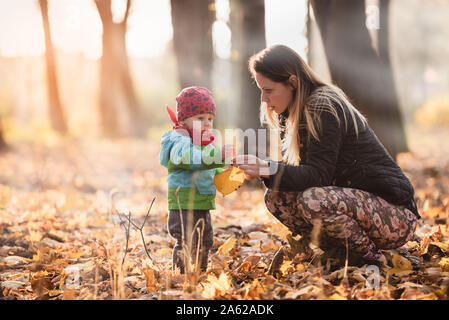 Mutter erzieht Ihr Kind an einem schönen Herbsttag. Mutter zeigt bunte Blätter. Baby Boy hält sie in seinen Händen. Die einzigartige Atmosphäre und Stimmung. Stockfoto