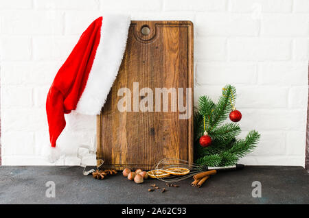 Weihnachten backen Hintergrund. Leer Schneidbrett mit Kochutensilien und Zutaten zum Kochen Backen auf leichte Küche. Santa's Hut und tanne Zweig Stockfoto