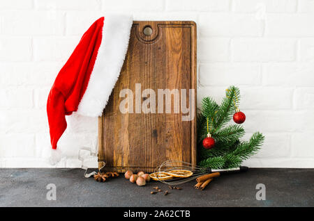 Weihnachten backen Hintergrund. Leer Schneidbrett mit Kochutensilien und Zutaten zum Kochen Backen auf leichte Küche. Santa's Hut und tanne Zweig Stockfoto