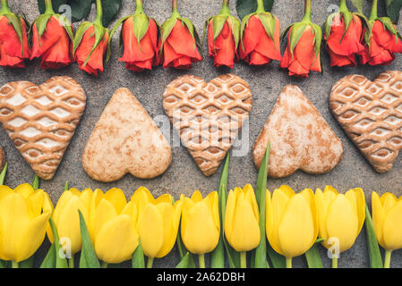 Frische und natürliche Tulpen und Rosen abwechselnd angeordnet mit handgefertigten Lebkuchen. Blumen und Süßigkeiten sind auf Moody Hintergrund angeordnet. Stockfoto