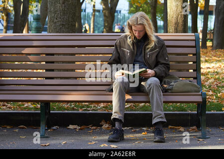 Charkow, Ukraine - Oktober 14, 2019: Der Kerl sitzt auf einer Bank im Herbst Park und liest Buch Stockfoto