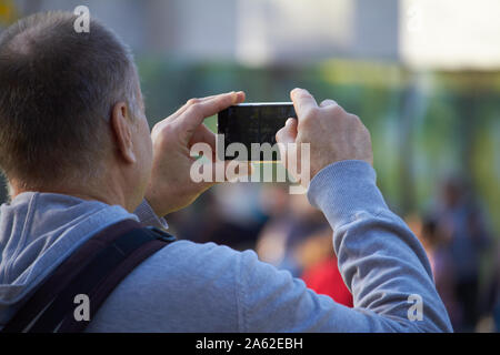 Charkow, Ukraine - Oktober 14, 2019: Männer auf der Straße fotografieren mit Handy, Hintergrund ist blured Stadt Stockfoto