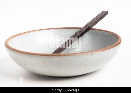 Ein paar traditionelle hölzerne Stäbchen mit einer leeren Steingut Schale. Stockfoto