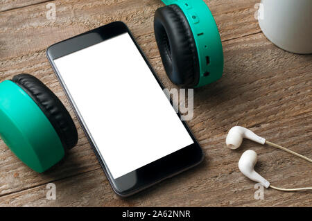 Leerer Bildschirm Smartphone auf Holztisch mit zwei verschiedenen Ohrhörer Stockfoto