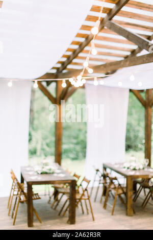 Verschwommenes Foto von Hochzeit Tische im Restaurant im Freien. Und Veranstaltungsräume. Die Tische und Stühle für Gäste, mit Laternen und Blumen geschmückt, serviert mit Stockfoto